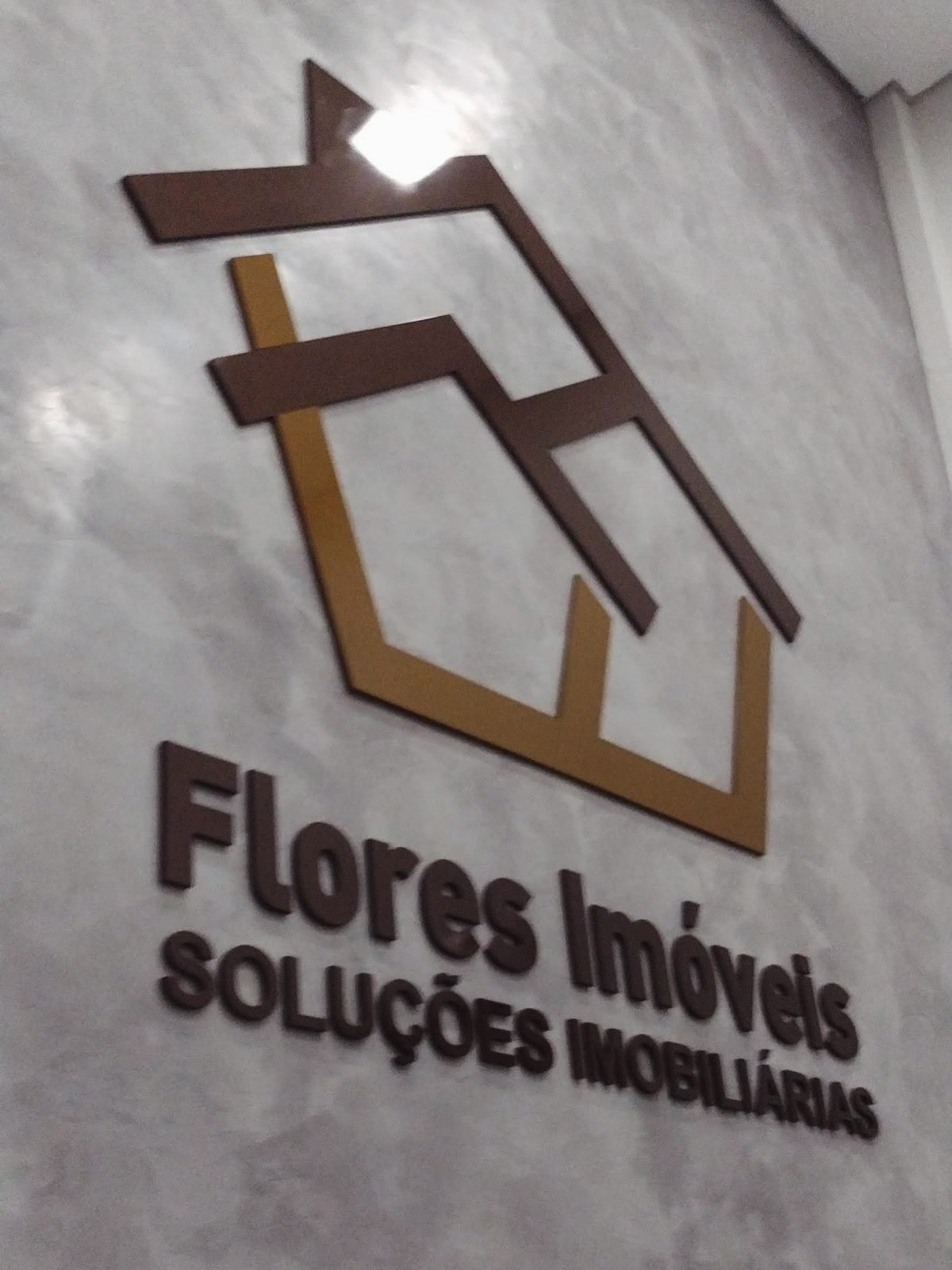 Letra caixa e símbolo em dois tons, instalados na parede interna da imobiliária.